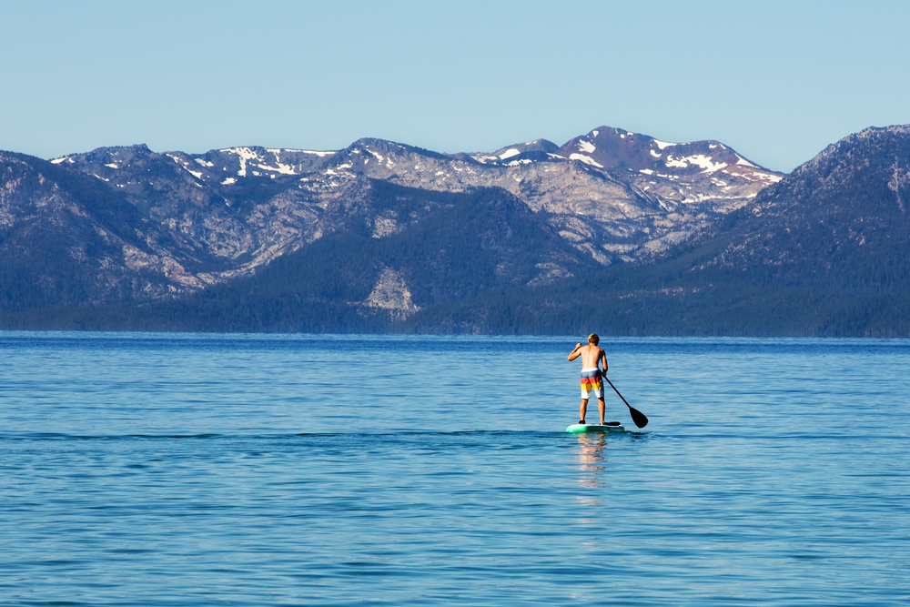 Featured image showing Man Paddle Boarding on Lake Tahoe with the Glow of the Sunrise on Him