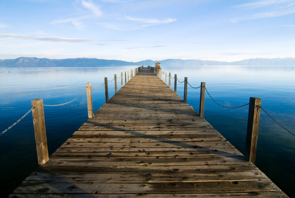 Featured image showing a long wooden pier on a crystal blue lake with mountains in the background